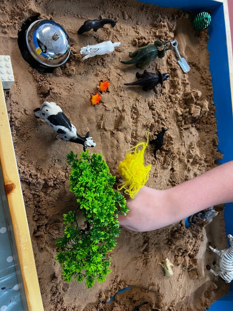 Hands playing in a sand tray with animal figures